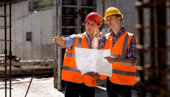 Civil engineer and construction manager in orange work vests and hard helmets explore construction